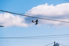 Shoes hanging from a powerline against white clouds, a plane flys away in the distance.
